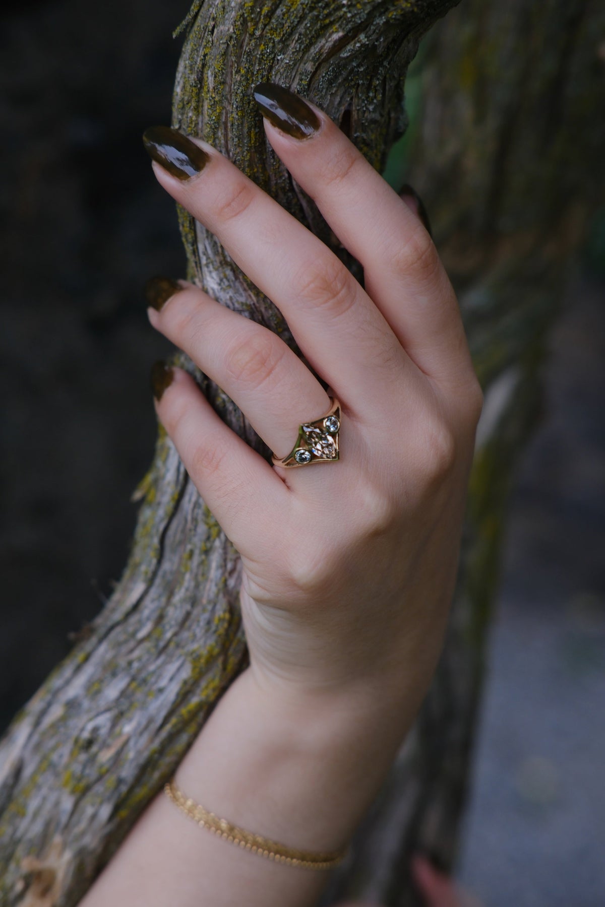 Model wears Champagne Triple Tributary Ring by Kestrel Dillon Jewelry over a log with blurred backdrop