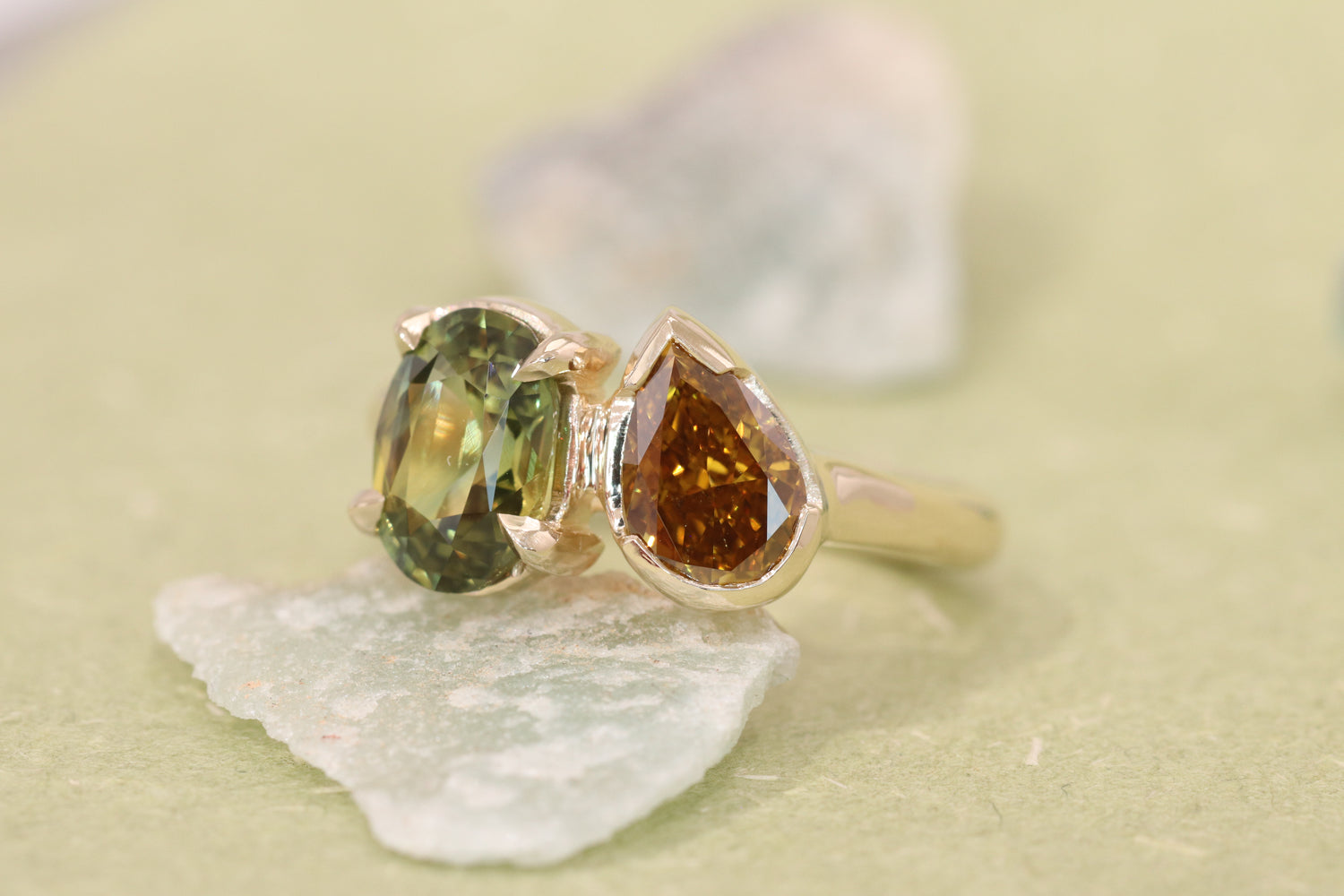 Custom 14k yellow gold ring with green and brown gemstones by Kestrel Dillon on a light background
