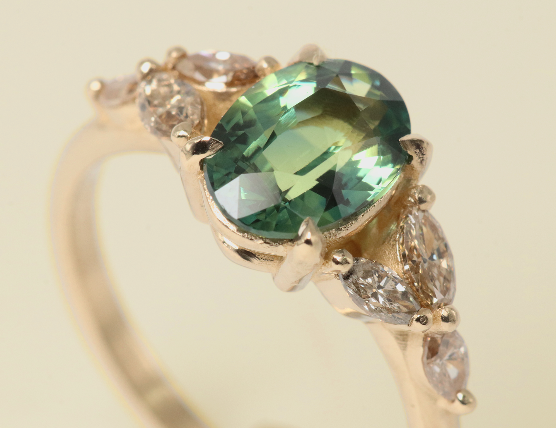 Angled view of the Aster Ring by Kestrel Dillon with a green center sapphire and smaller diamonds on a beige background
