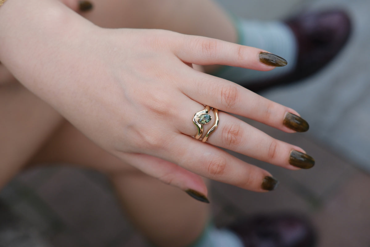 Model wears Sapphire Root Ring stacked with Root Curve Band on middle finger with blurred backdrop